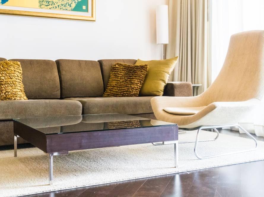 Living room with a brown sofa, mustard cushions, glass coffee table and a cream lounge chair