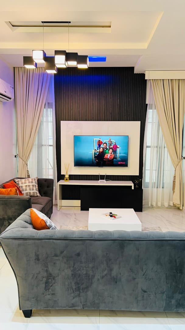 Living room with a charcoal media wall, cove lighting, velvet sofa and cream drapes