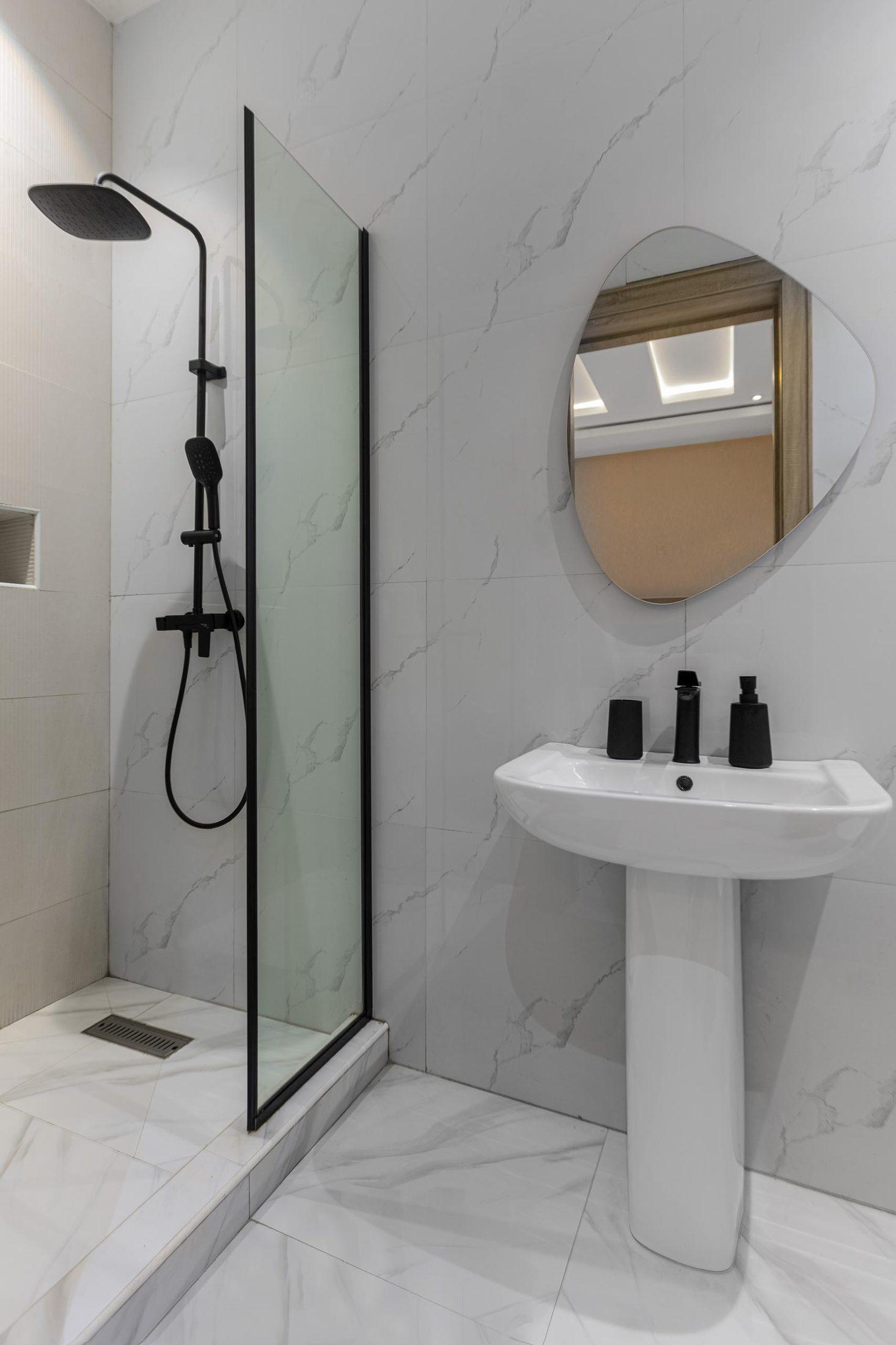 Marble-tiled shower room with a glass screen, rainfall shower, pedestal basin and oval mirror