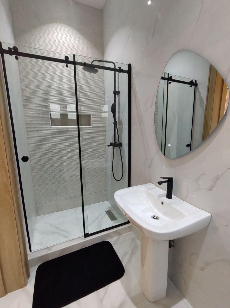 Walk-in shower with sliding glass door, matt black fittings, pedestal basin and organic mirror