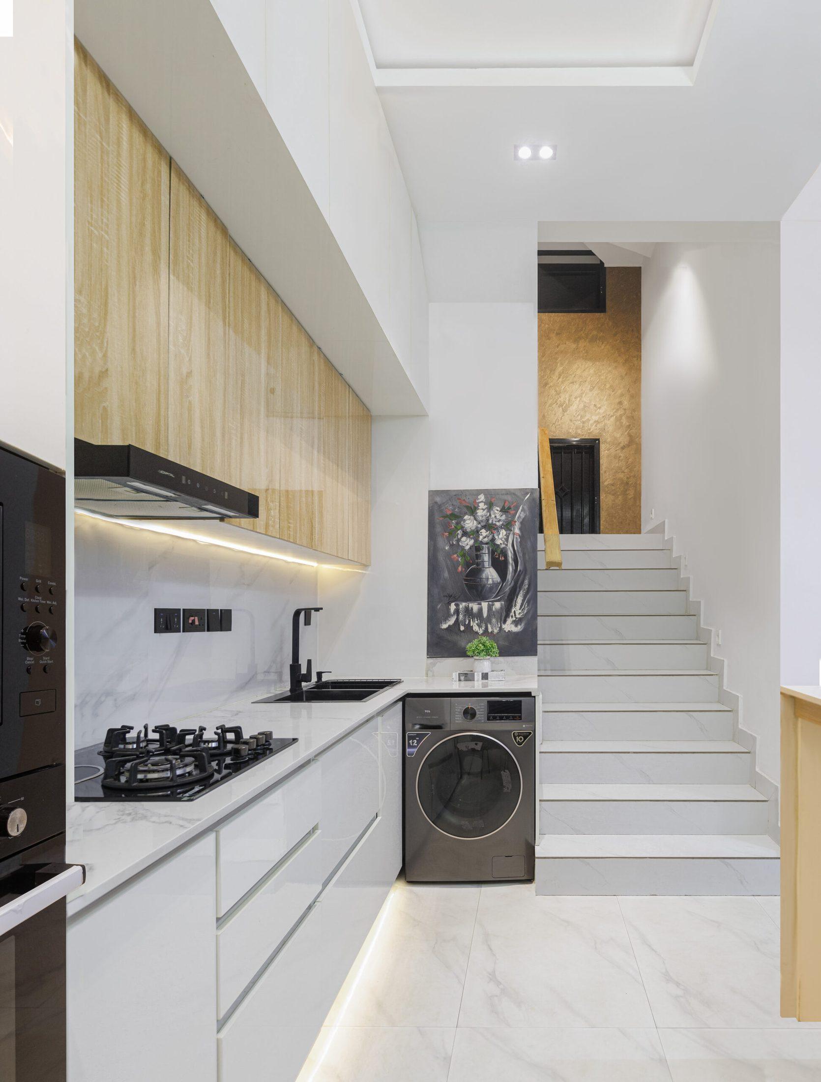 White gloss and oak kitchen with under-cabinet lighting, integrated appliances and a staircase beyond