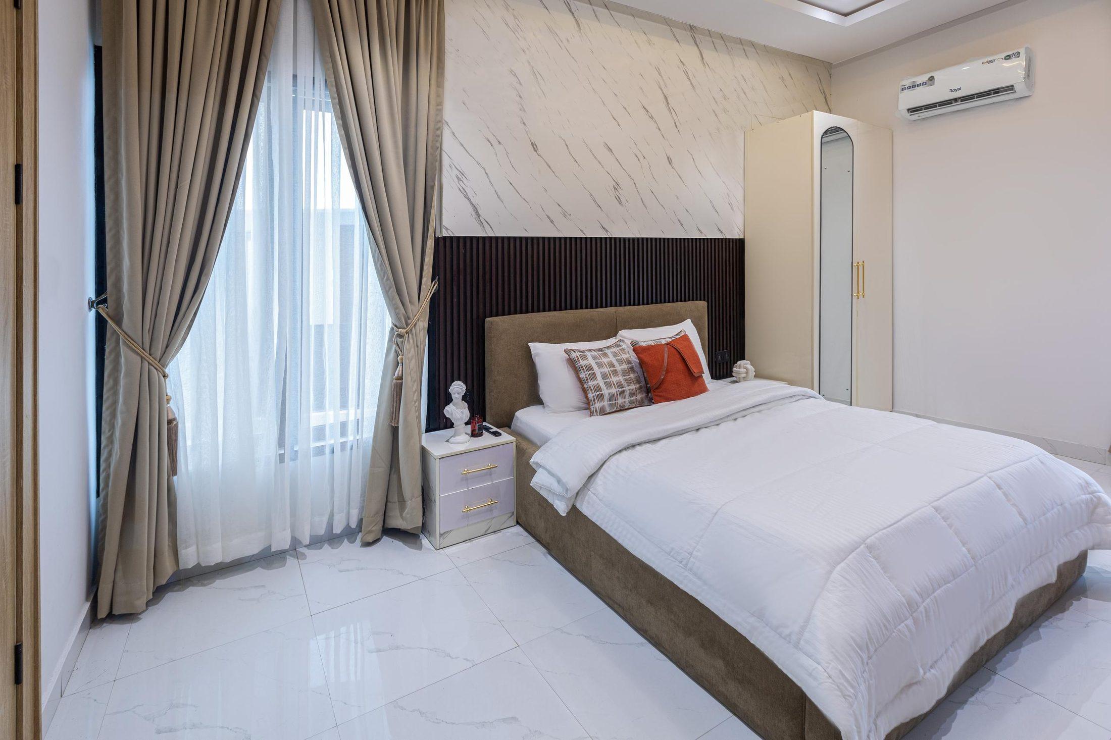Guest bedroom with a slatted headboard wall, marble-effect accent wall and layered neutral bedding