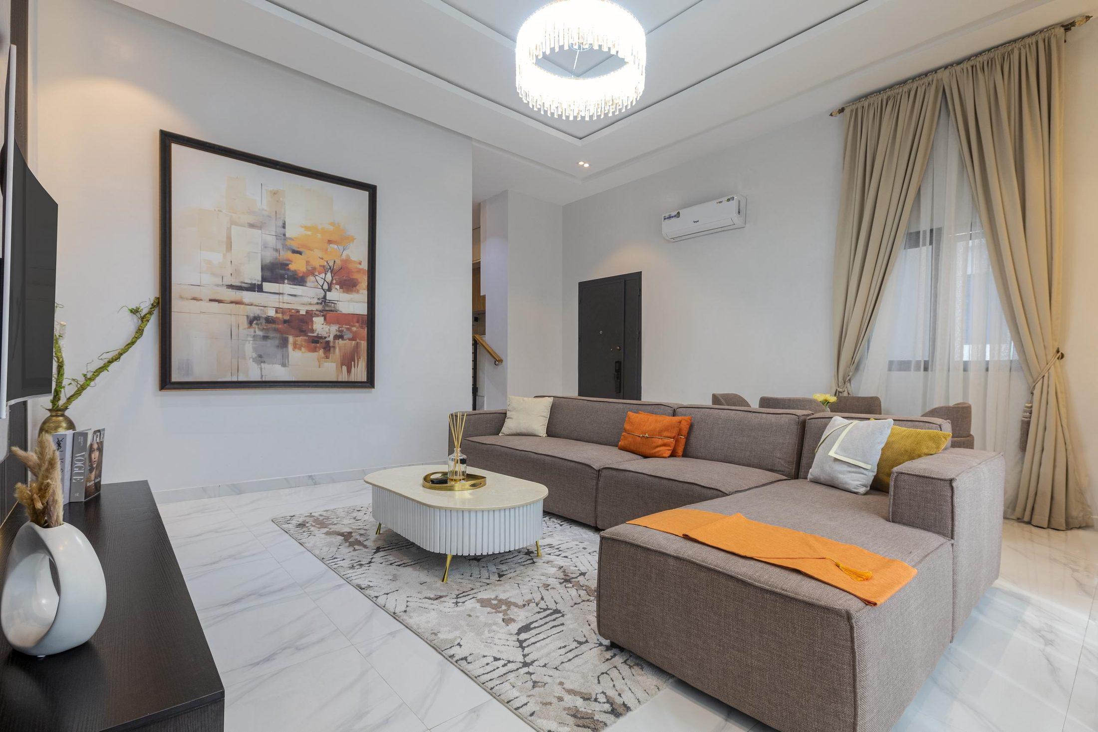 Bright lounge with a taupe sectional sofa, oval coffee table, abstract artwork and floor-length curtains